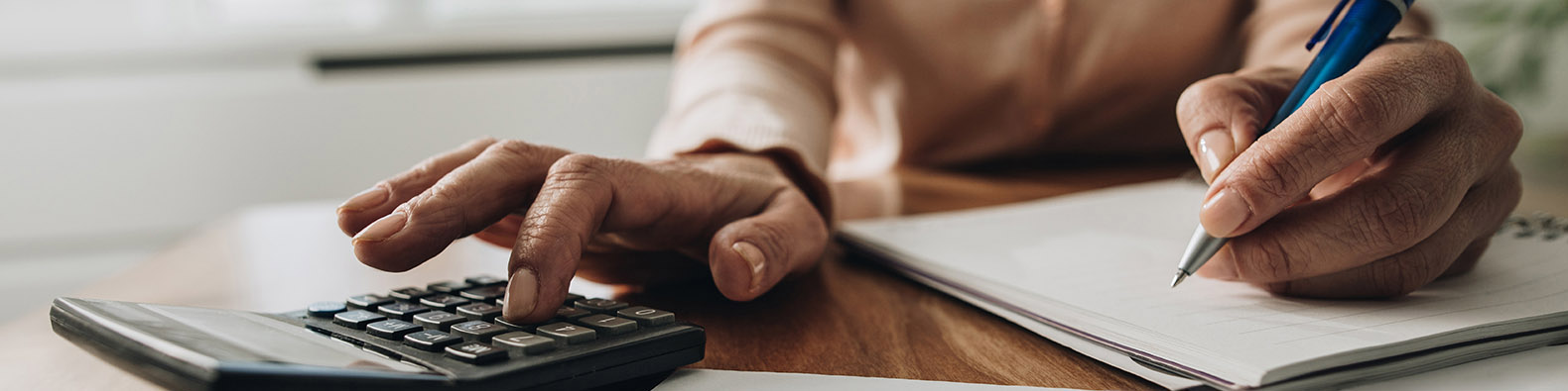 Close up of unrecognizable woman using calculator while going through bills and home finances.